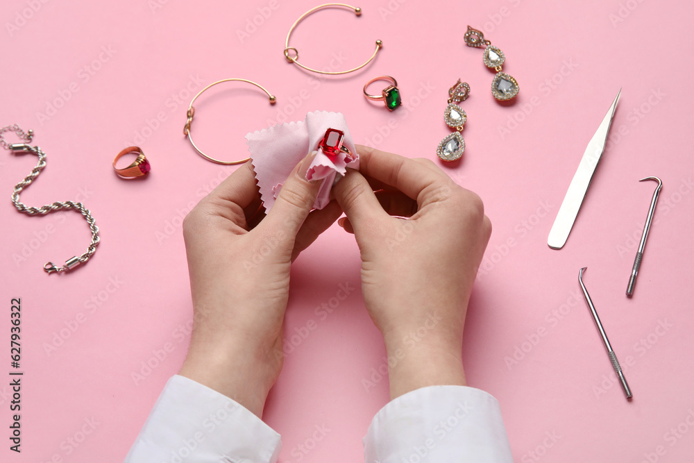 Woman cleaning beautiful jewelry on pink background, closeup