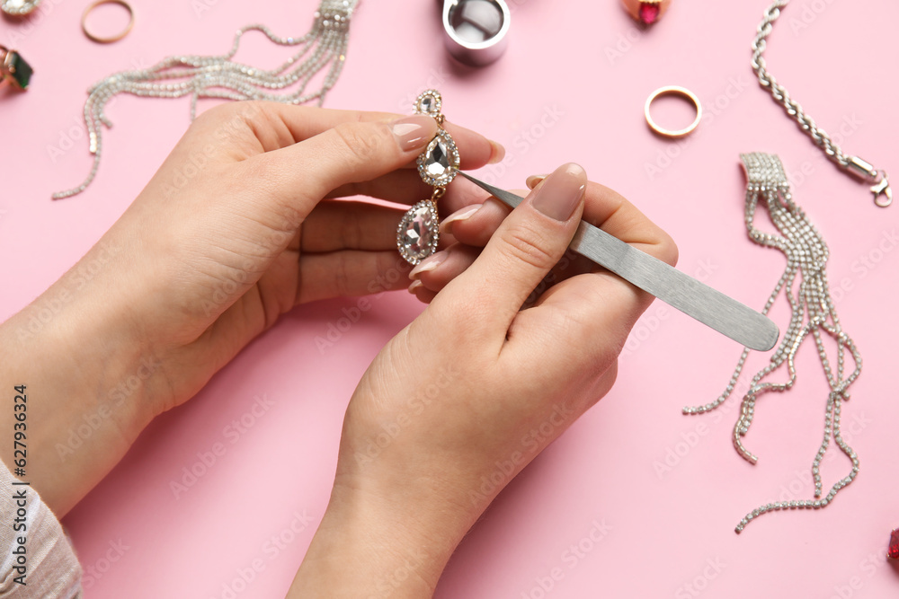 Woman cleaning beautiful earring on pink background, closeup