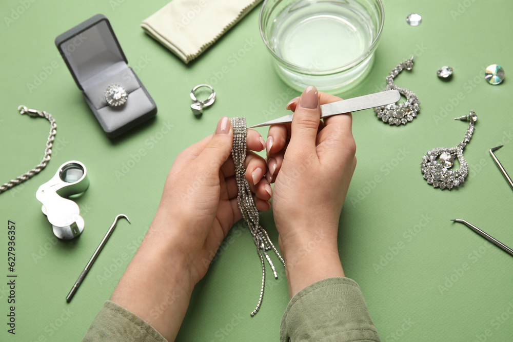 Woman cleaning beautiful jewelry on green background, closeup