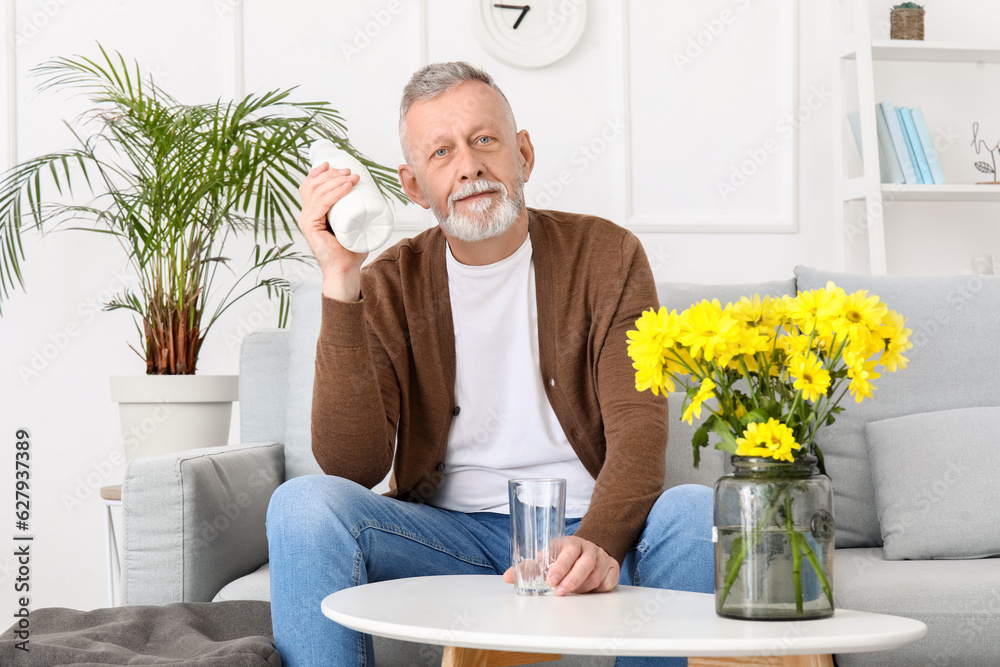 Mature man with glass and bottle of milk at home