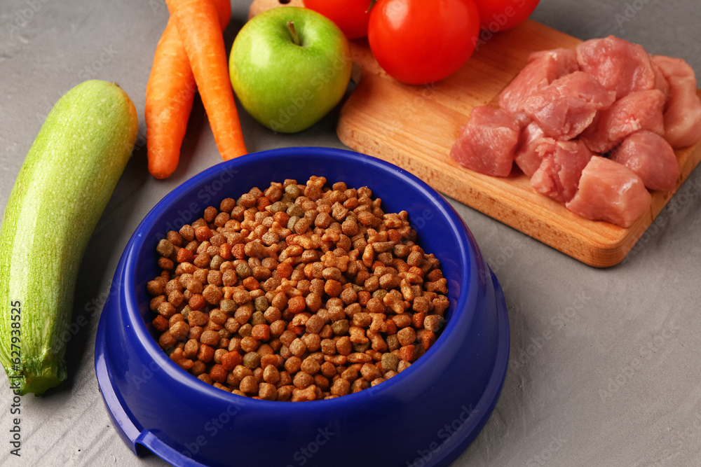 Bowl with dry pet food, raw meat and natural products on color wooden background, closeup