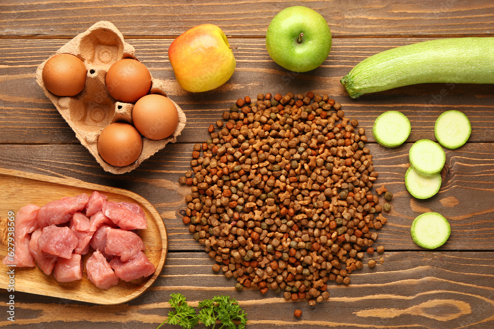 Dry pet food, raw meat and natural products on wooden background