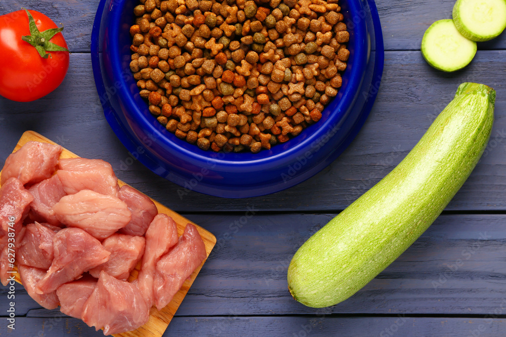 Bowl with dry pet food, raw meat and natural products on color wooden background, closeup