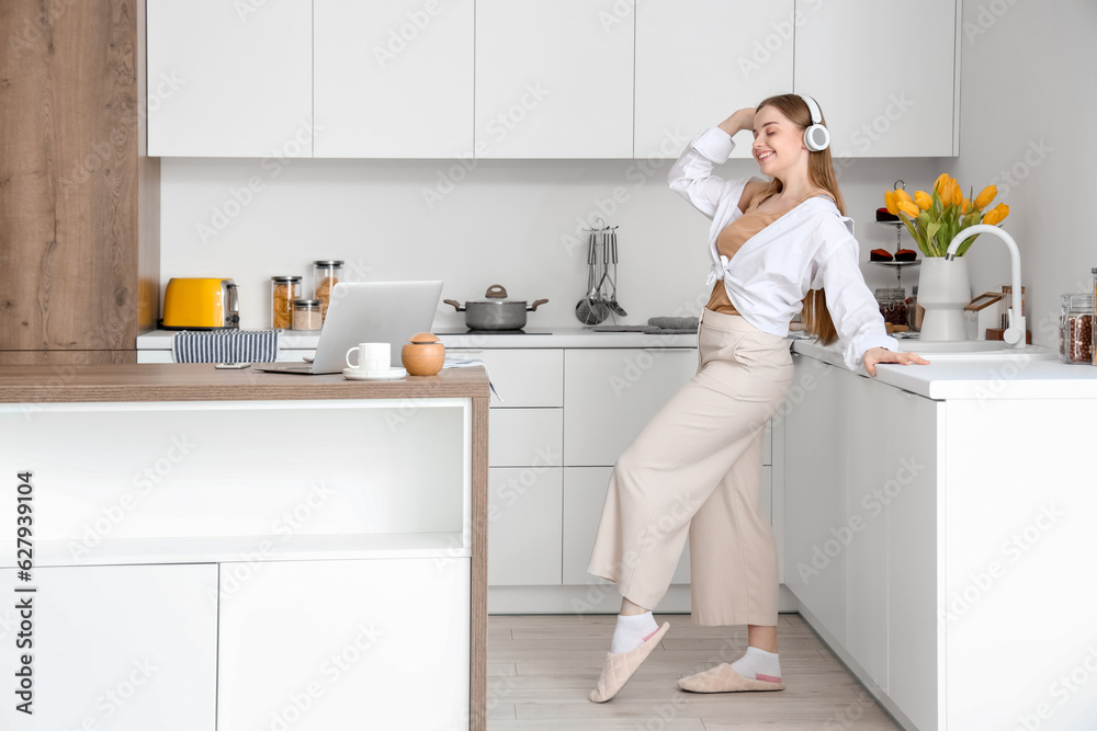 Happy young woman listening to music in modern kitchen