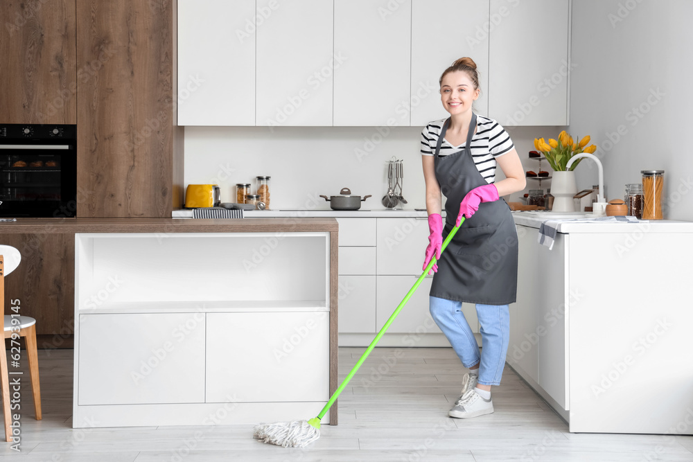 Happy young woman mopping floor in light kitchen