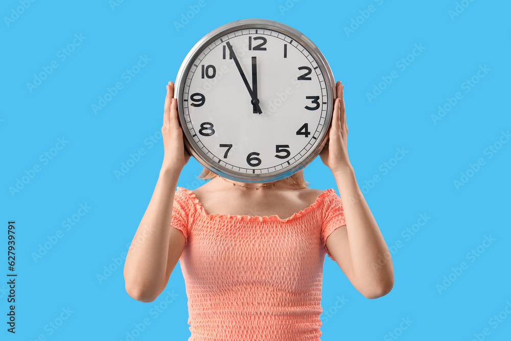 Young woman with clock on blue background. Deadline concept