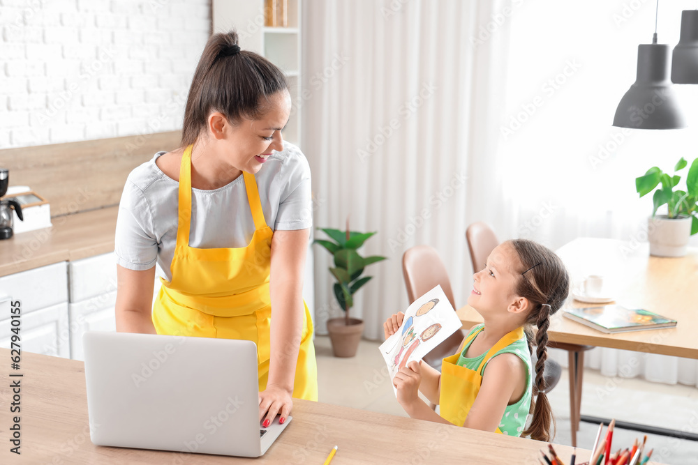 Little girl showing drawing to her working mother in kitchen