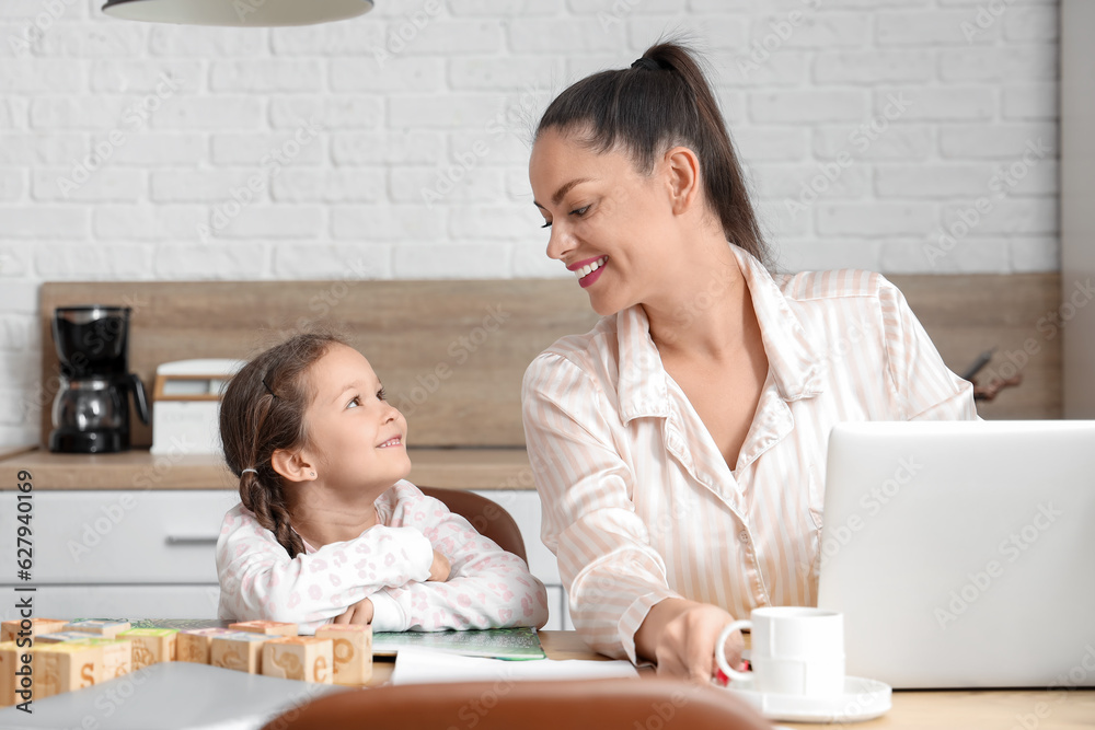 Working mother with her little daughter reading book in kitchen