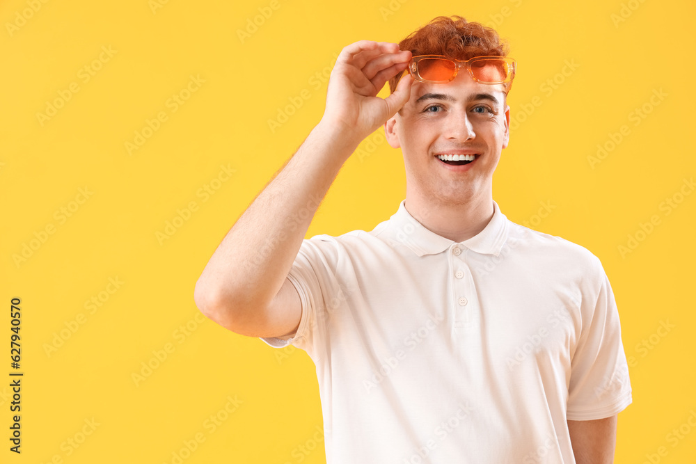 Young redhead man in stylish sunglasses on yellow background