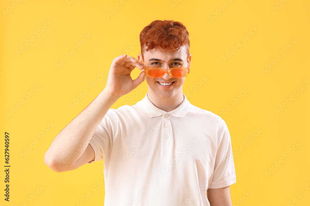 Young redhead man in stylish sunglasses on yellow background