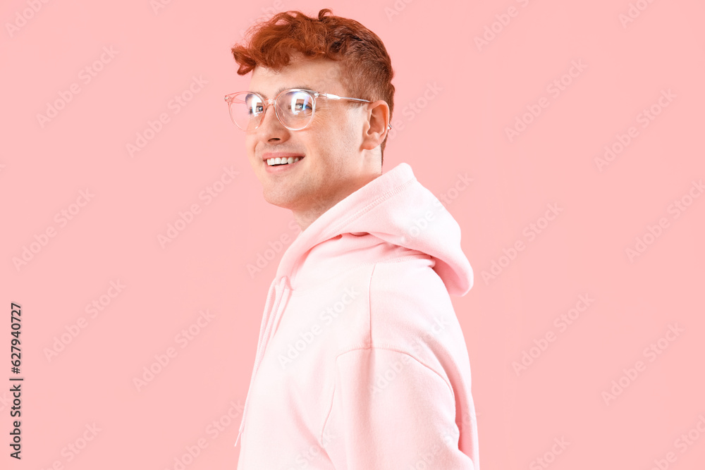 Young redhead man in eyeglasses on pink background