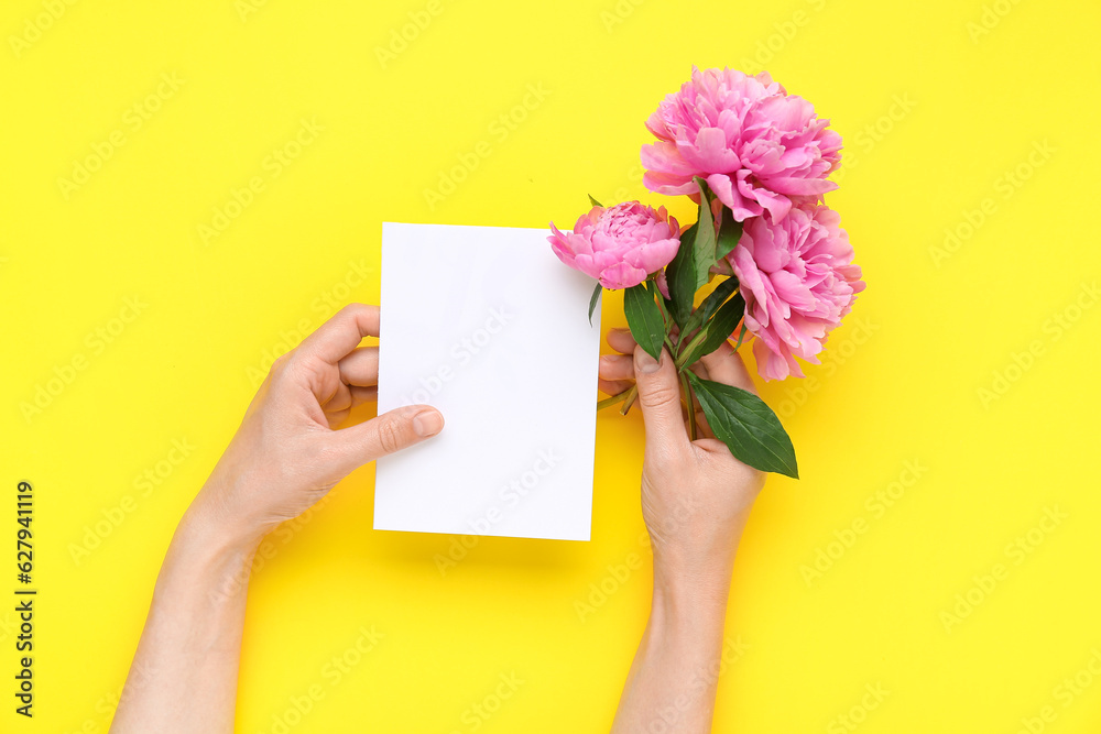 Female hands with blank card and beautiful peony flowers on yellow background