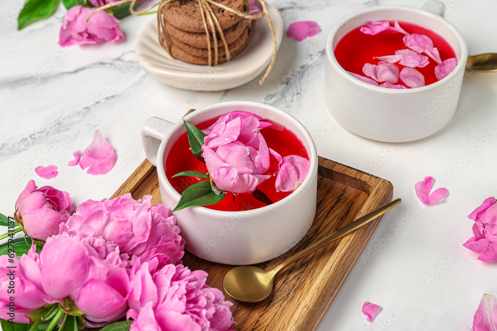 Cups of tea and beautiful peony flowers on light background, closeup