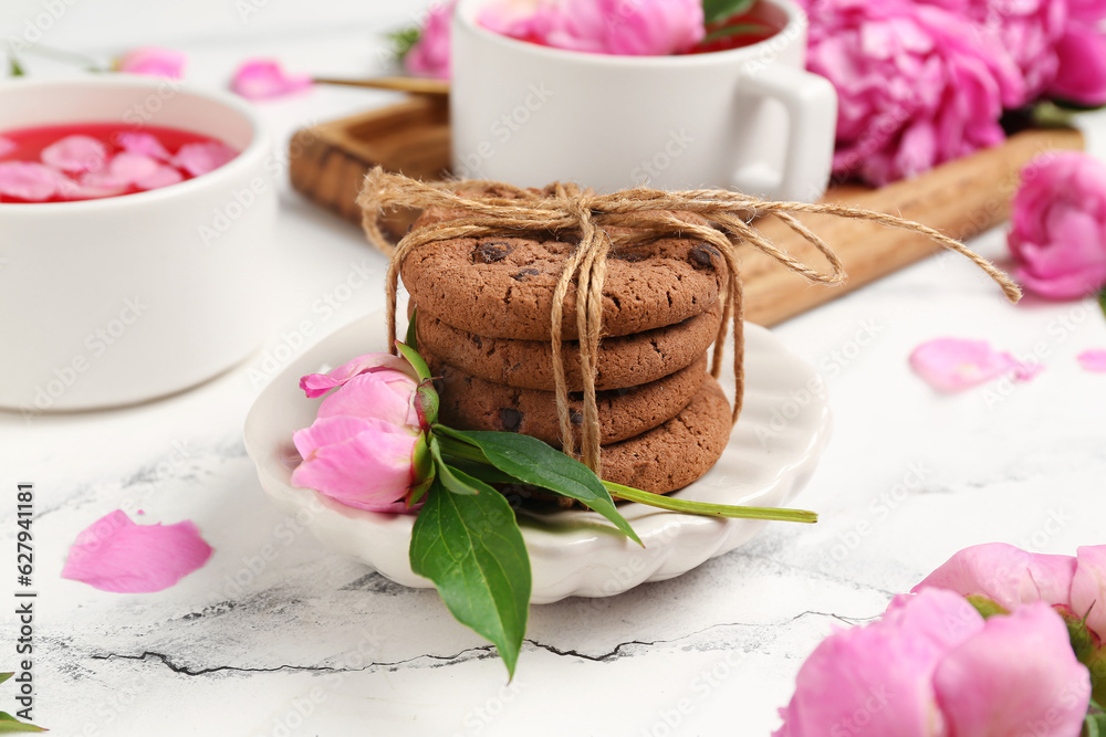 Plate with sweet cookies and beautiful peony flowers on light background