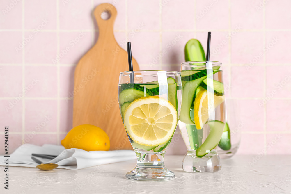 Glasses of lemonade with cucumber on white table near pink tile wall