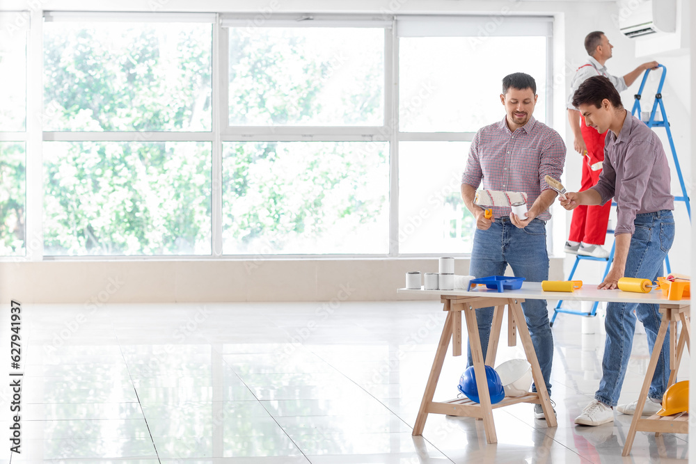 Male builders with paint can and rollers working in room