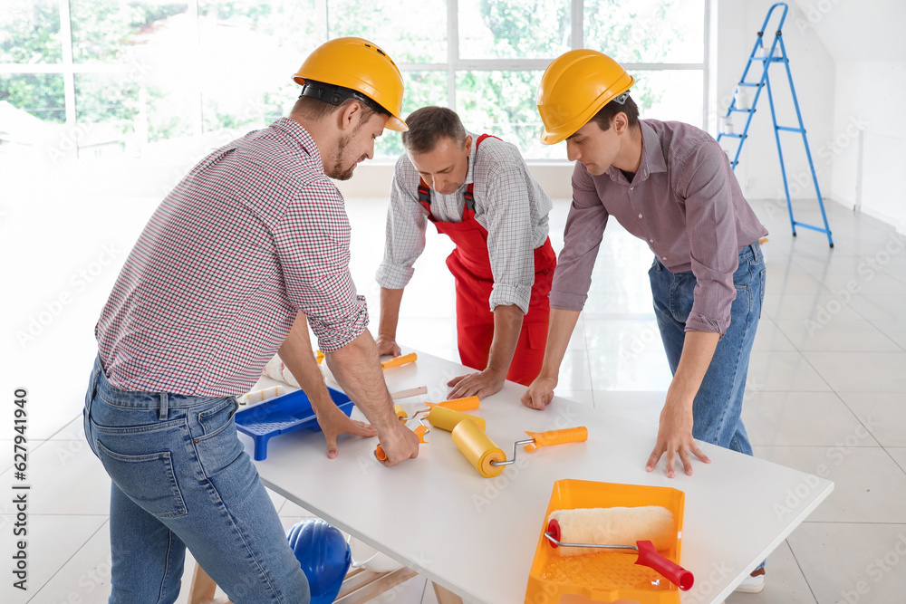 Team of male builders with paint rollers working in room