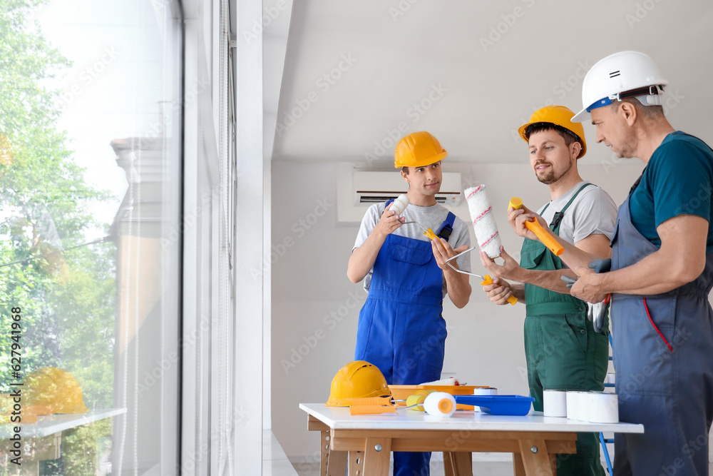 Team of male builders with paint rollers working in room