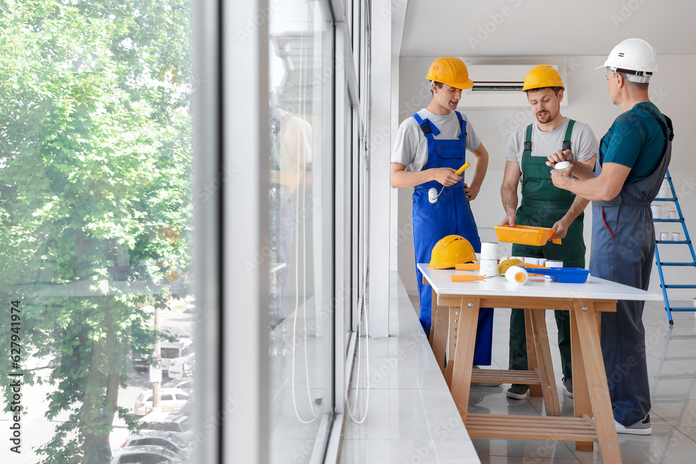 Team of male builders with paint rollers working in room