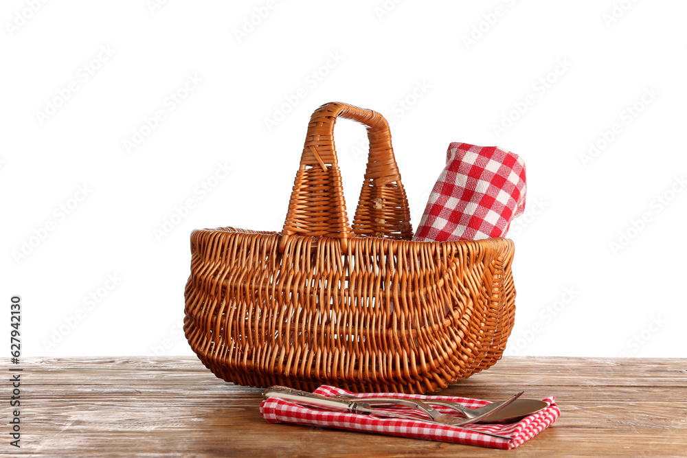 Wicker picnic basket with napkin and cutlery on wooden table against white background