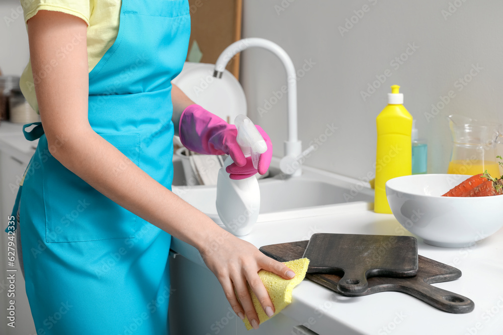 Young woman cleaning counter with sponge in kitchen, closeup