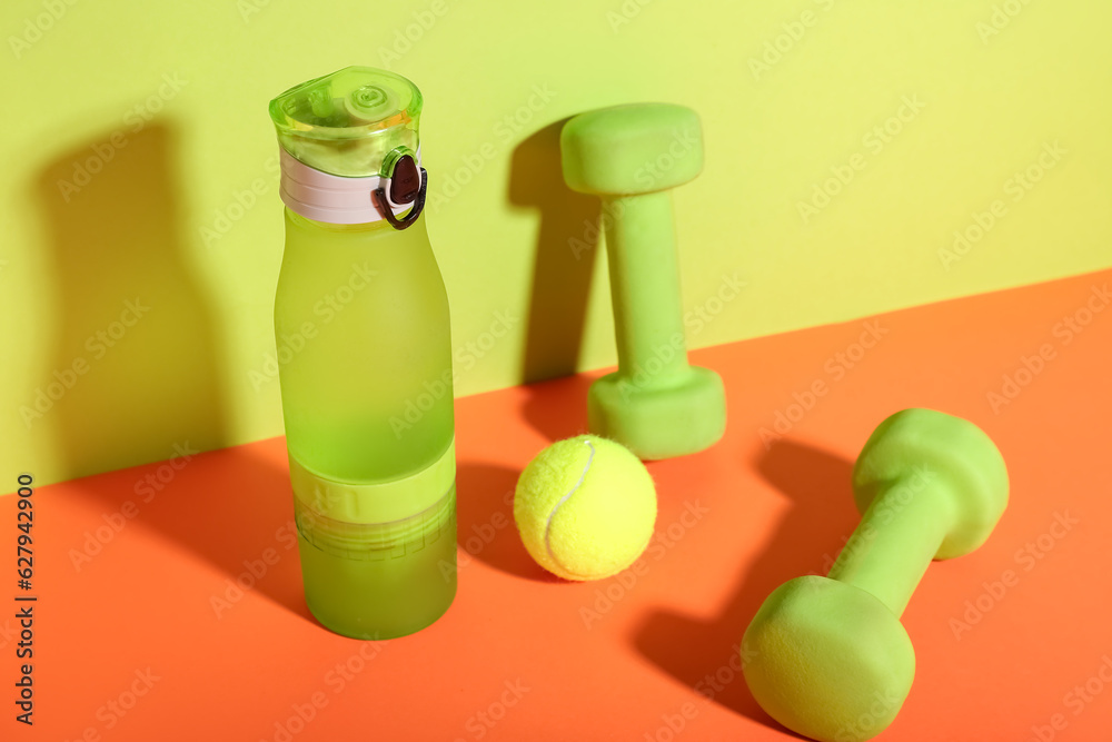 Bottle of water, dumbbells and tennis ball on color background