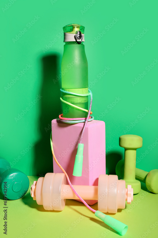 Set of sports equipment with bottle of water on green background