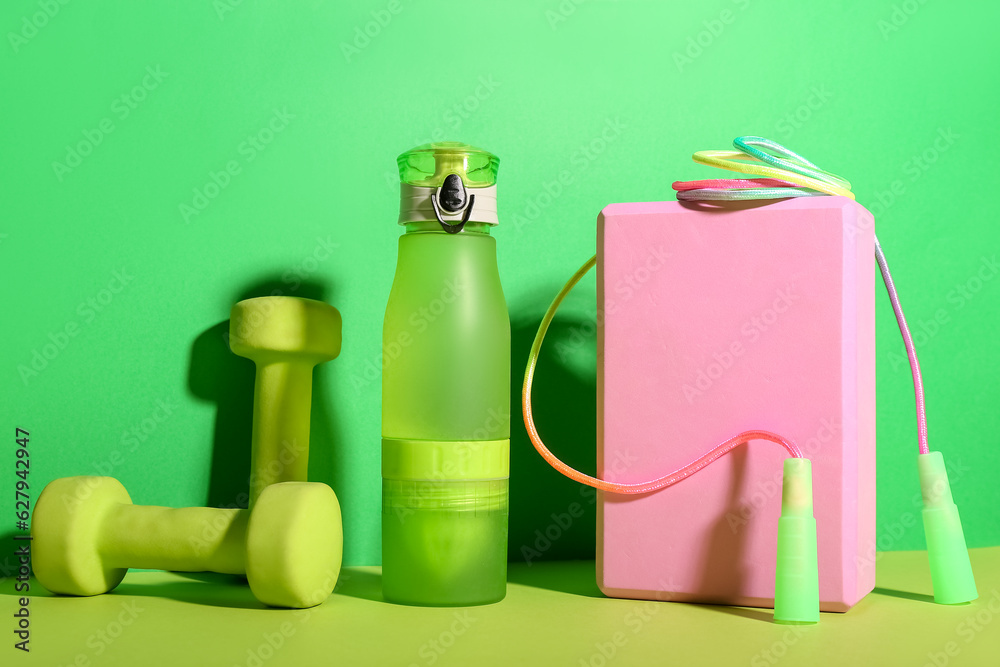 Set of sports equipment with bottle of water on green background