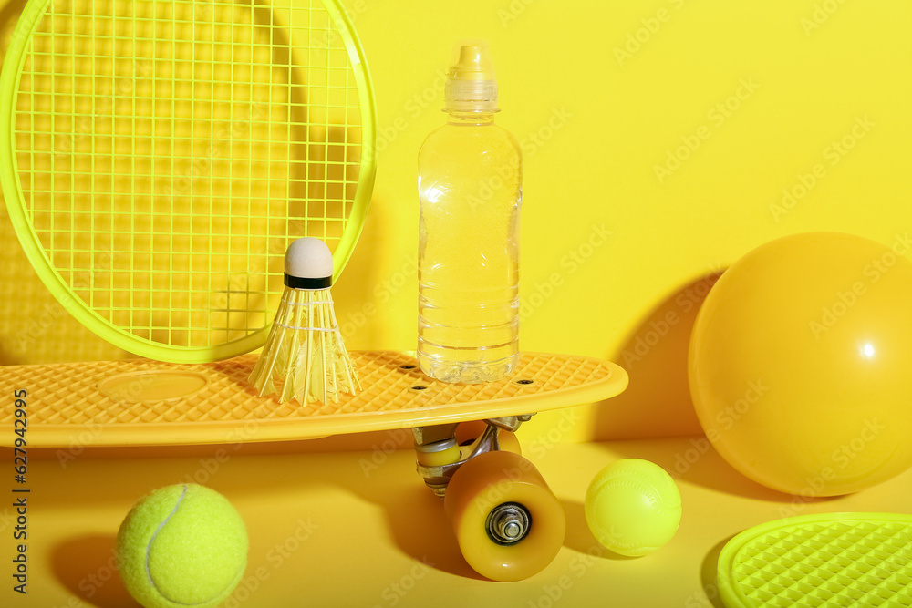 Set of sports equipment with bottle of water on yellow background