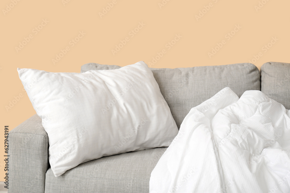 Grey sofa with white pillow and blanket near beige wall