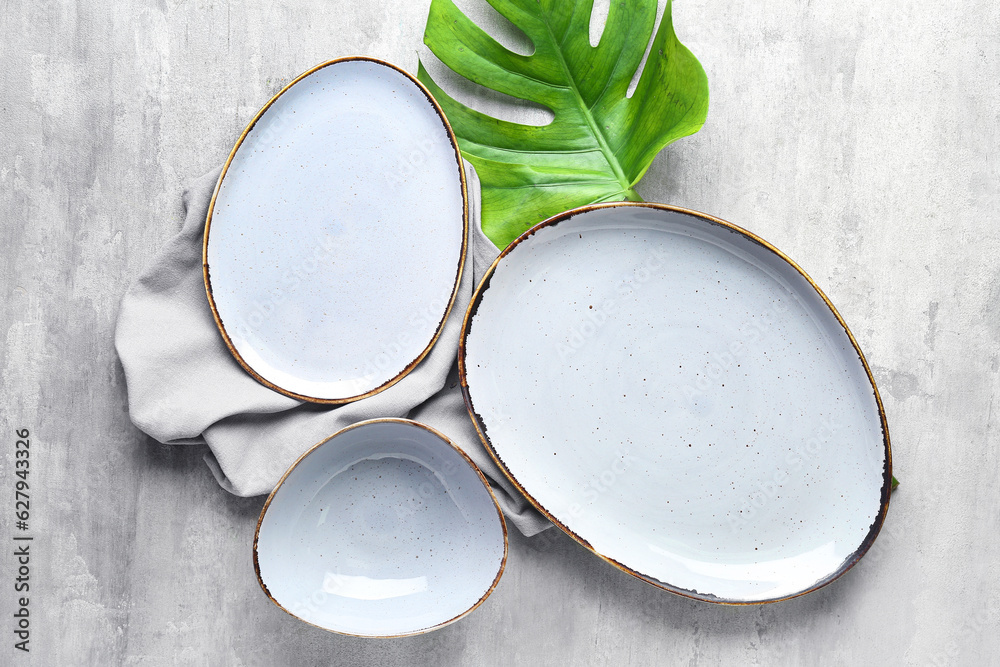 Set of clean plates and monstera leaf on grey table