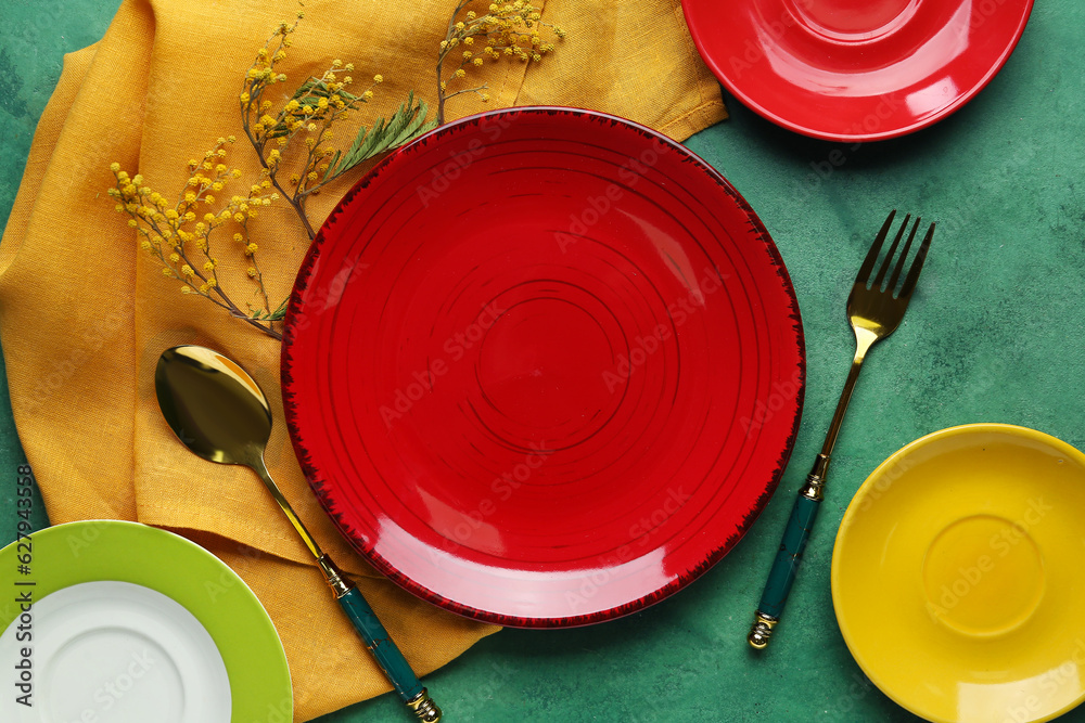 Table setting with colorful plates, golden cutlery and floral decor on green background