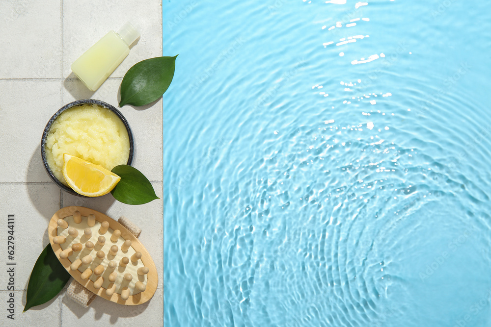 Lemon body scrub with massage brush and cosmetic bottle on edge of swimming pool