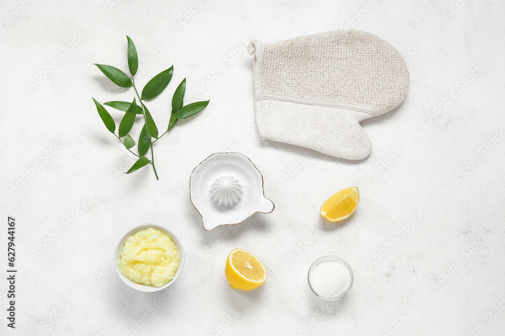 Bowl of lemon body scrub with massage glove and juicer on white background