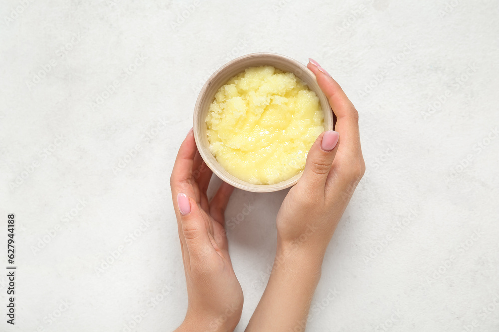 Female hands with bowl of lemon body scrub on white background