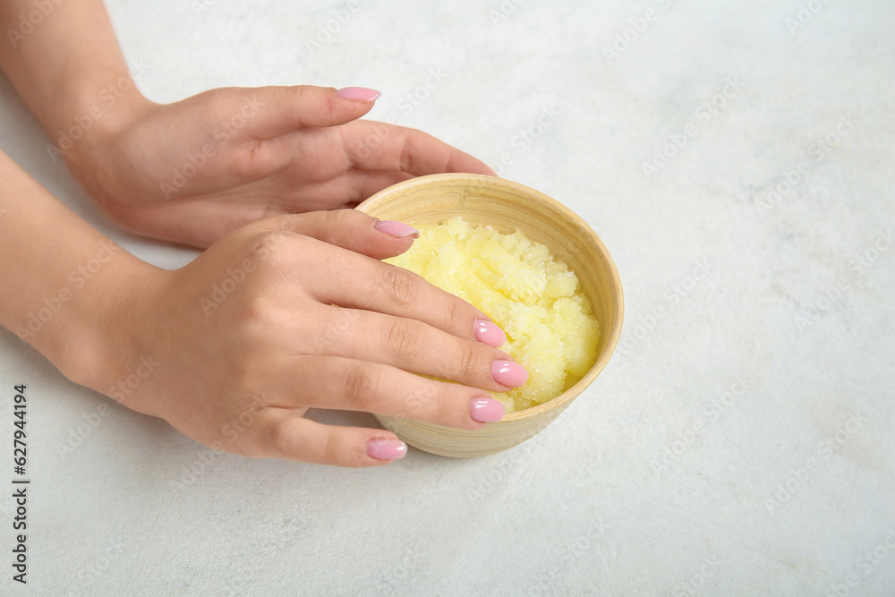 Female hands with bowl of lemon body scrub on white background