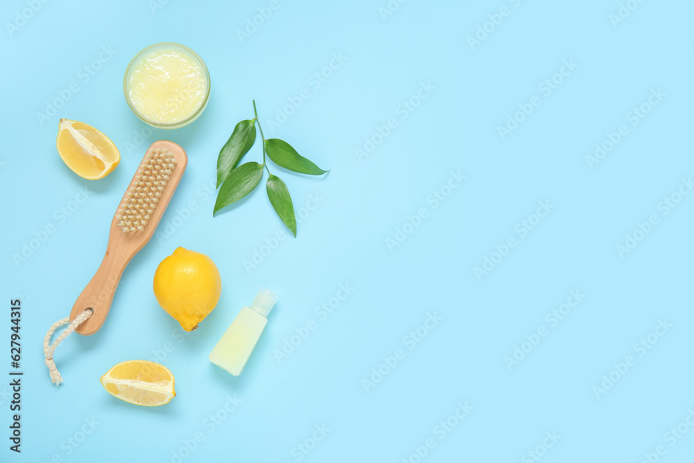 Bowl of lemon body scrub with massage brush and cosmetic bottle on blue background