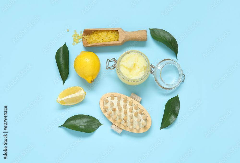 Jar of lemon body scrub with massage brush and sea salt on blue background