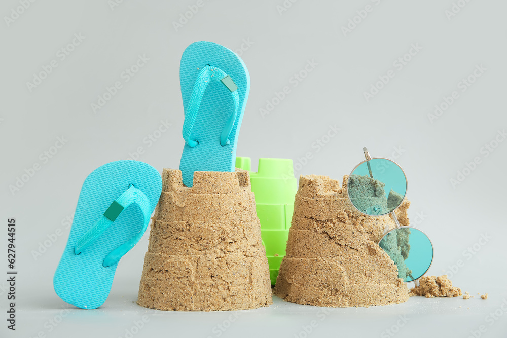 Castle made of sand with beach accessories and toy bucket on grey background