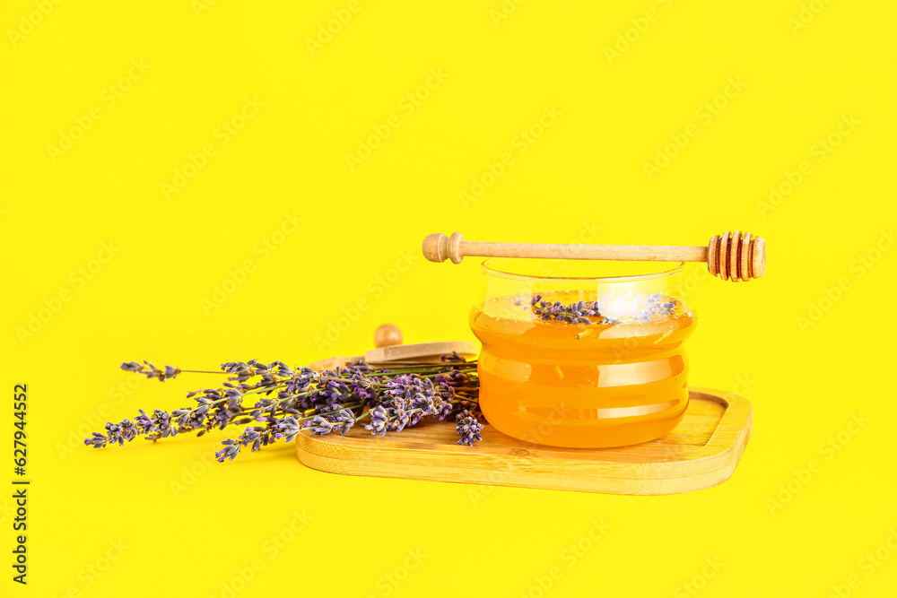 Wooden board with jar of sweet lavender honey, dipper and flowers on yellow background