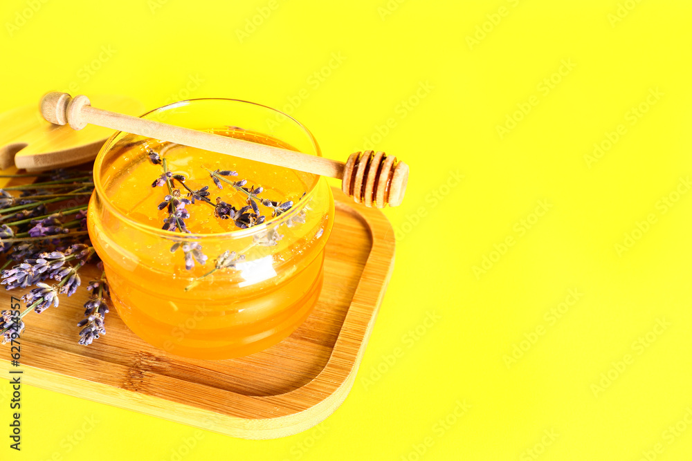 Wooden board with jar of sweet lavender honey, dipper and flowers on yellow background