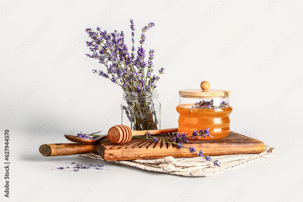 Wooden board with jar of sweet lavender honey, dipper and flowers on white background