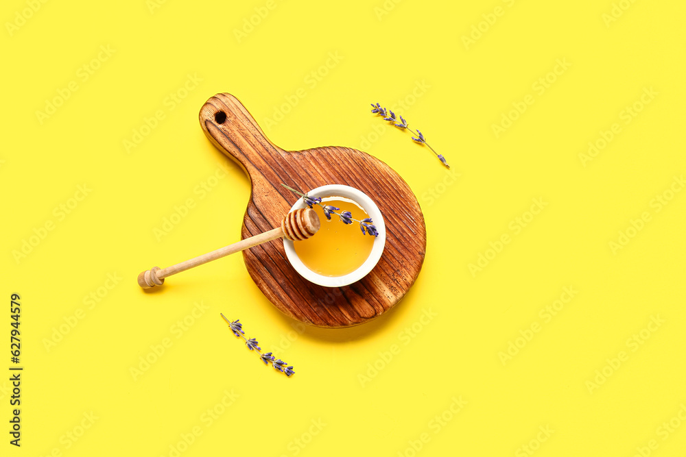 Wooden board with bowl of sweet lavender honey, dipper and flowers on yellow background