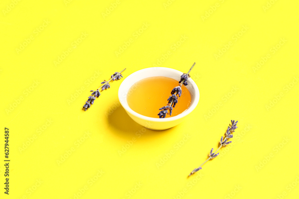 Bowl of sweet lavender honey and flowers on yellow background