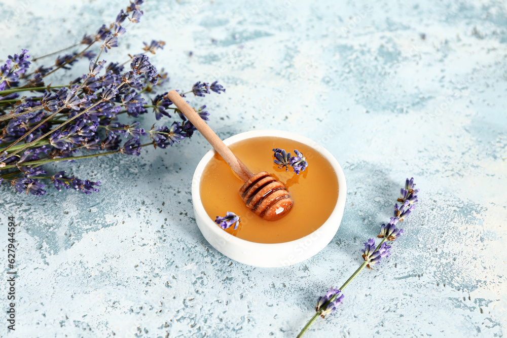 Bowl of sweet lavender honey, dipper and flowers on blue background