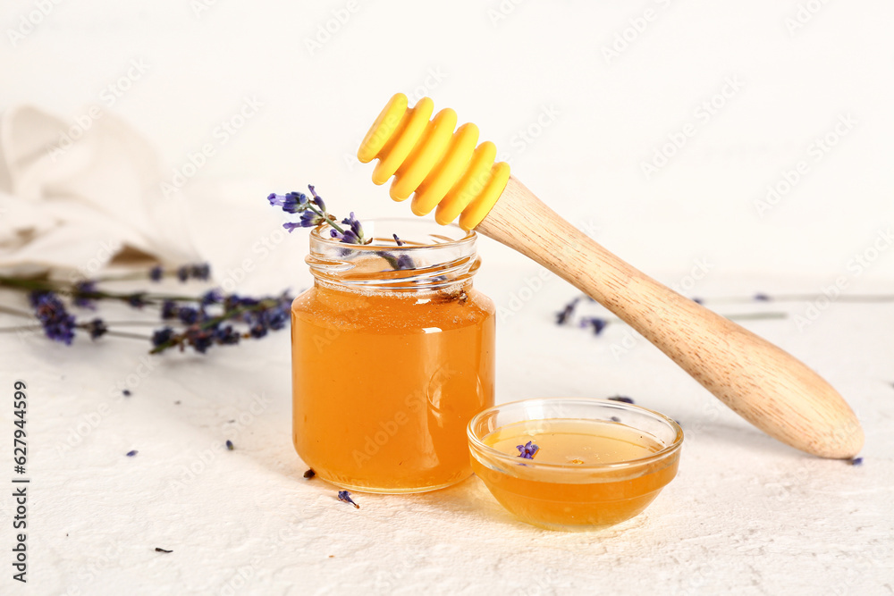 Jar and glass bowl of sweet lavender honey with flowers on white background