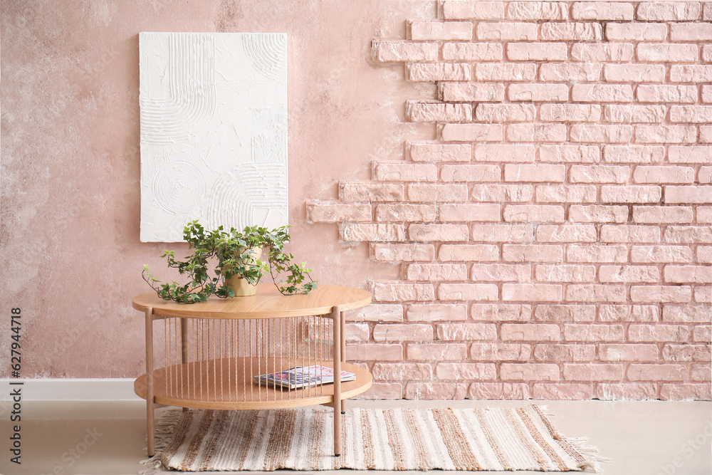 Wooden coffee table with houseplant in room near pink brick wall