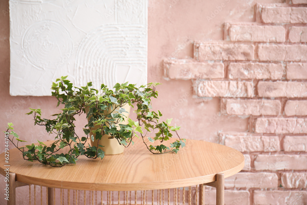 Wooden coffee table with houseplant in room near pink brick wall