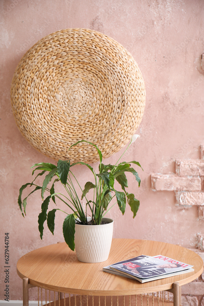 Wooden coffee table with magazines and houseplant in room near pink brick wall