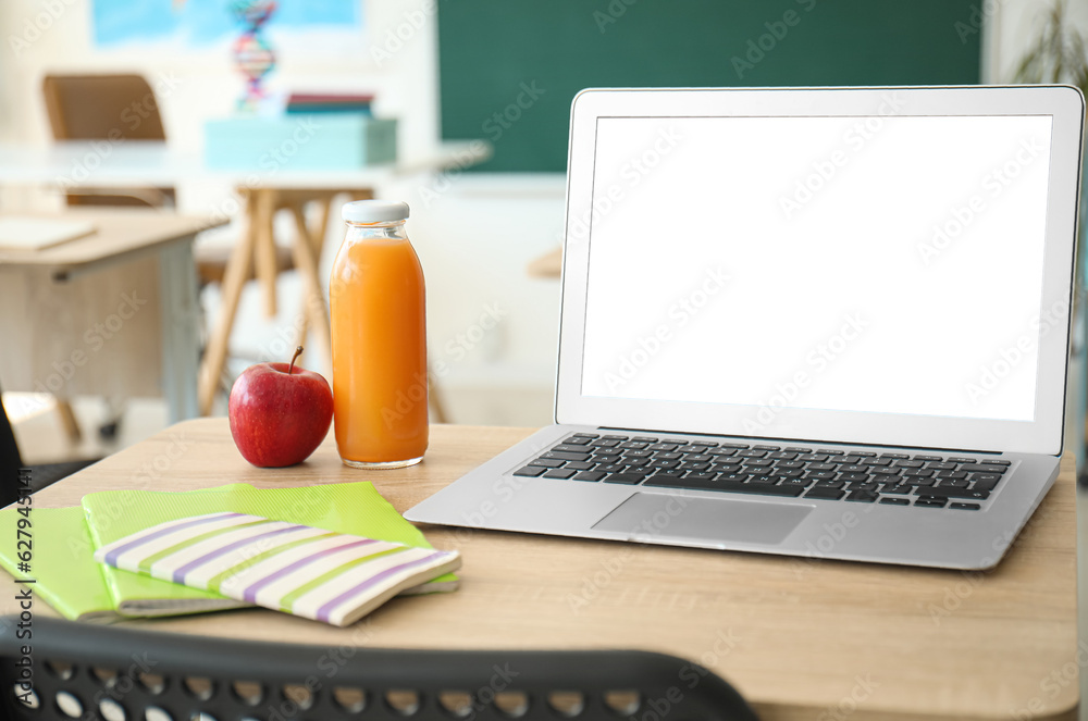 Laptop with lunch and stationery on desk in classroom